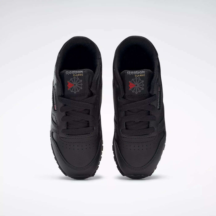 A pair of Kids' Classic Leather Shoes - Preschool by Reebok in black are shown from above, highlighting the leather uppers, laces, and Reebok logos on the tongues against a plain white background.