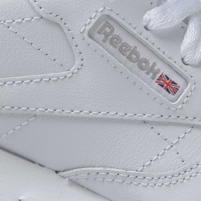Close-up of Reebok Kids' Classic Leather Shoes - Preschool in white, showcasing a leather upper, detailed stitching, Reebok branding, and a small Union Jack flag on the side.