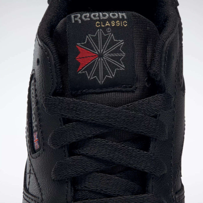 Close-up of the tongue and laces of the Kids' Classic Leather Shoes - Preschool by Reebok, featuring a black leather upper, white and gold Reebok branding, and a bold red-and-white star design.