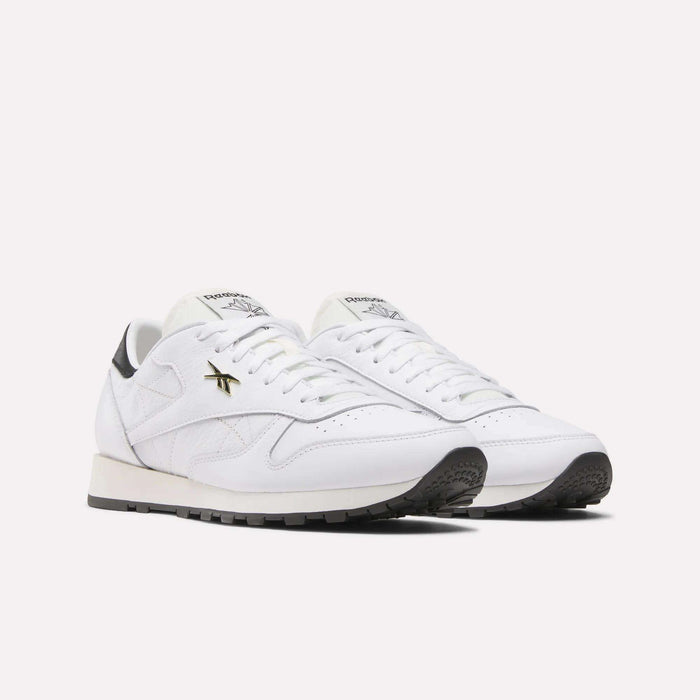 The Reebok Classic Leather Shoes showcase a retro running style with a white leather upper, black soles, gold logo accents, and white laces, set against a plain light background.