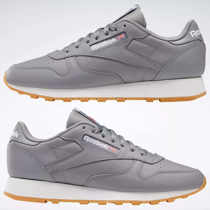 The Reebok Classic Leather Shoes feature gray leather uppers, white midsoles, and light brown rubber outsoles. Seen from the side against a plain background, they display the Reebok logo and UK flag on the sides.