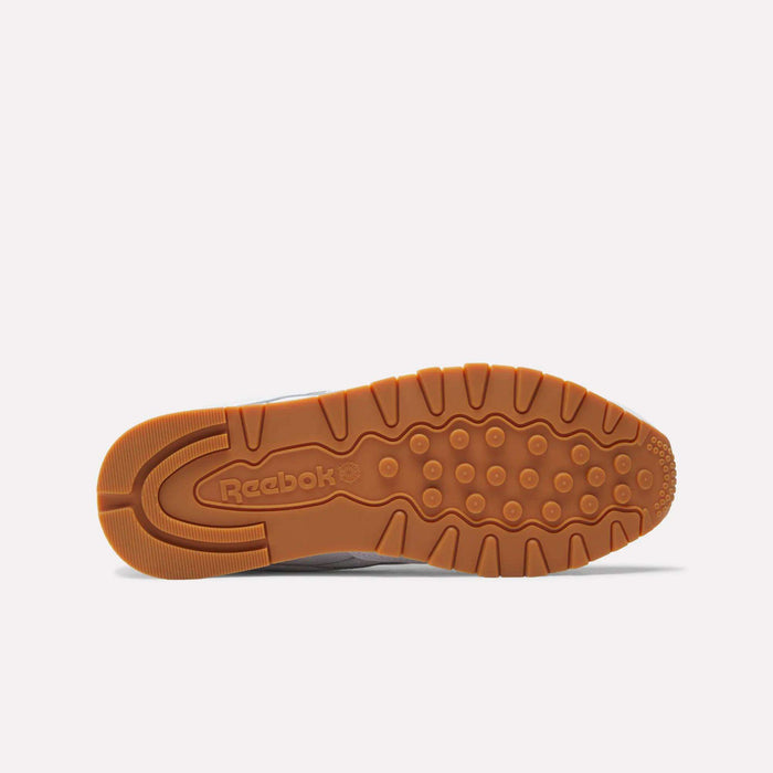The image displays the bottom view of Reebok Classic Leather Shoes, showcasing a tan rubber sole with circular grip patterns and an embossed Reebok logo in the center, set against a plain white background.
