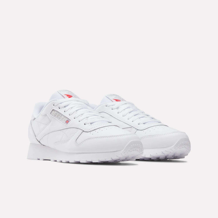 The Reebok Classic Leather Shoes feature a minimal design with a leather upper, white laces, and subtle red Reebok branding on the tongue and side, shown against a plain light background.