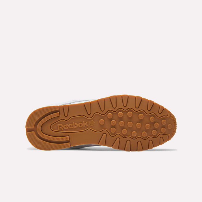 The image displays the bottom view of Reebok Classic Leather Shoes with a brown rubber sole, textured grip patterns, and the Reebok logo embossed near the heel, showcasing its retro-inspired design.