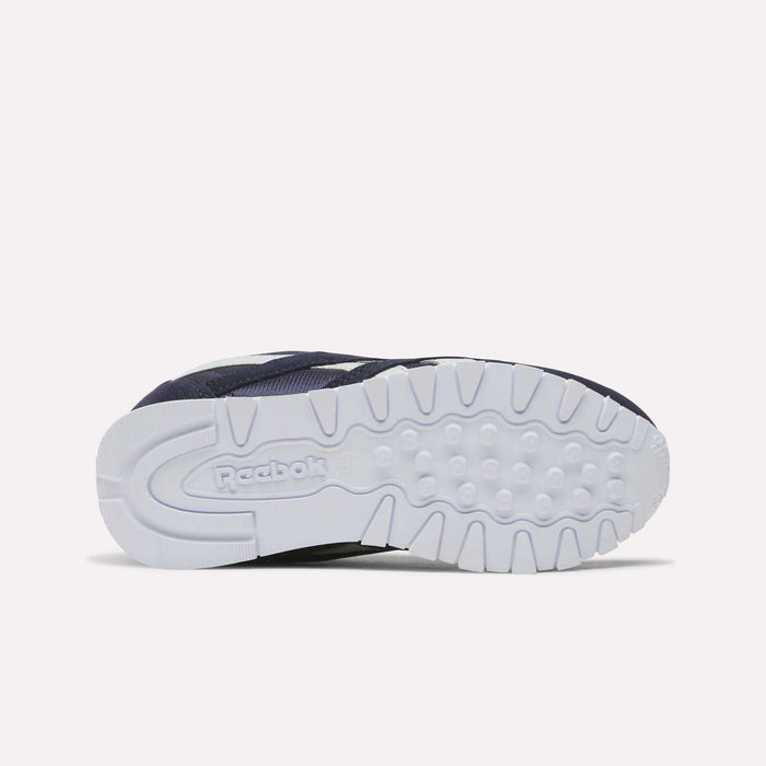 The image displays the bottom sole of the Reebok Classic Nylon Shoes for little kids, showcasing a white rubber outsole with textured grip patterns and the Reebok logo embossed near the heel. Inspired by classic nylon styles, these shoes offer both comfort and timeless appeal—perfect for boys.