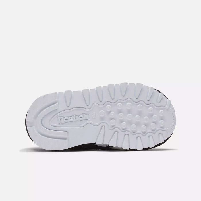The image displays the sole of the Reebok Kids' Classic Nylon Shoes - Toddler, featuring a white rubber outsole with textured grips and an embossed Reebok logo, known for comfort and durability among toddler boys' footwear.