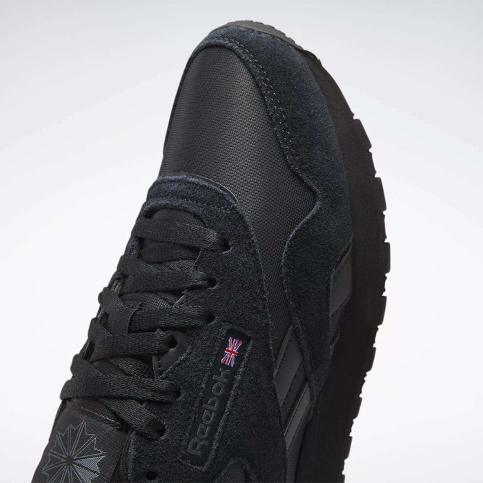Close-up of the Reebok Men's Classic Nylon Shoes in black, featuring a suede and nylon upper, laces, Reebok logo with UK flag, thick rubber sole, and a star-shaped design near the toe for a classic everyday look.