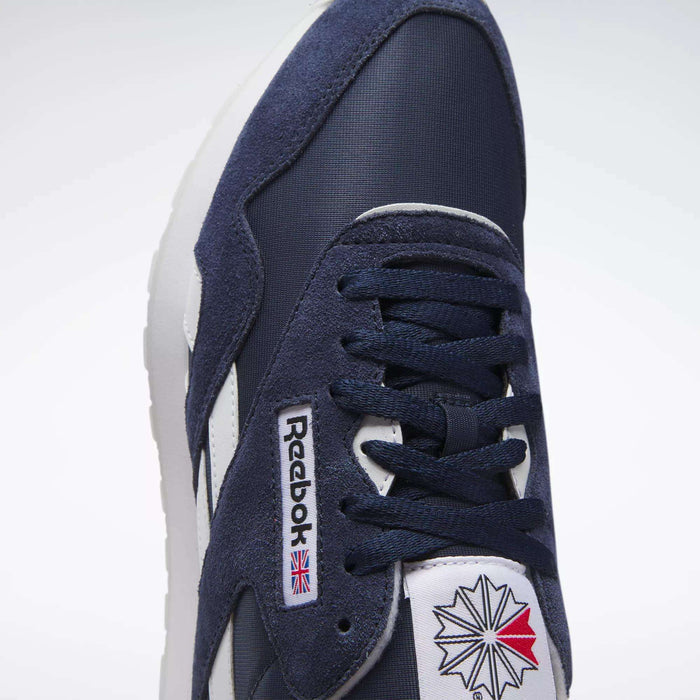 Close-up of Reebok Men's Classic Nylon Shoes in navy blue and white, featuring a nylon upper, laces, the iconic logo tag with UK flag, and a red-white-blue geometric tongue design—timeless everyday sneakers.