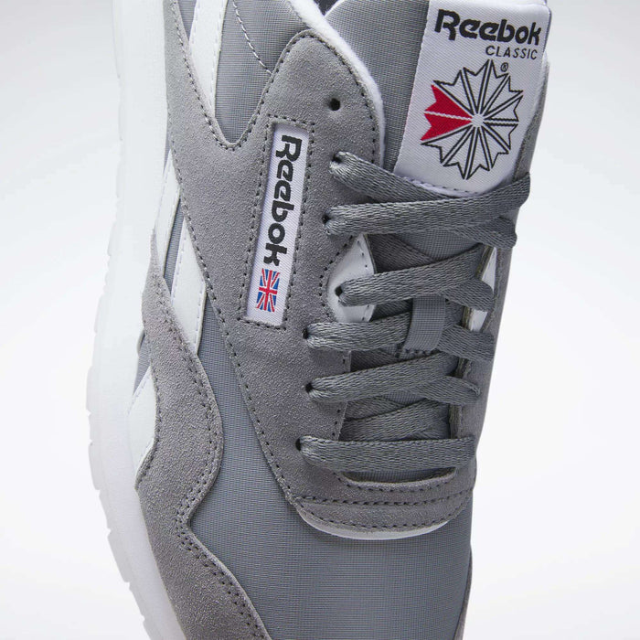A close-up of Reebok Men's Classic Nylon Shoes with a grey nylon upper, white stripes, laces, Reebok branding, and a red, white, and blue geometric design on the tongue for classic everyday style.