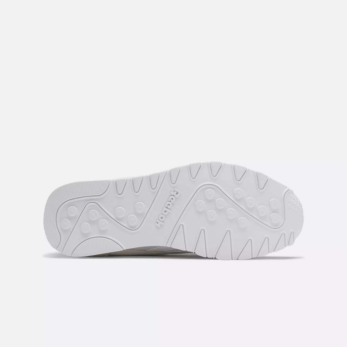 The image displays the white rubber outsole of Reebok Men's Classic Nylon Shoes, featuring circular grips, wavy lines, and the embossed Reebok logo at the center on a plain light gray background.