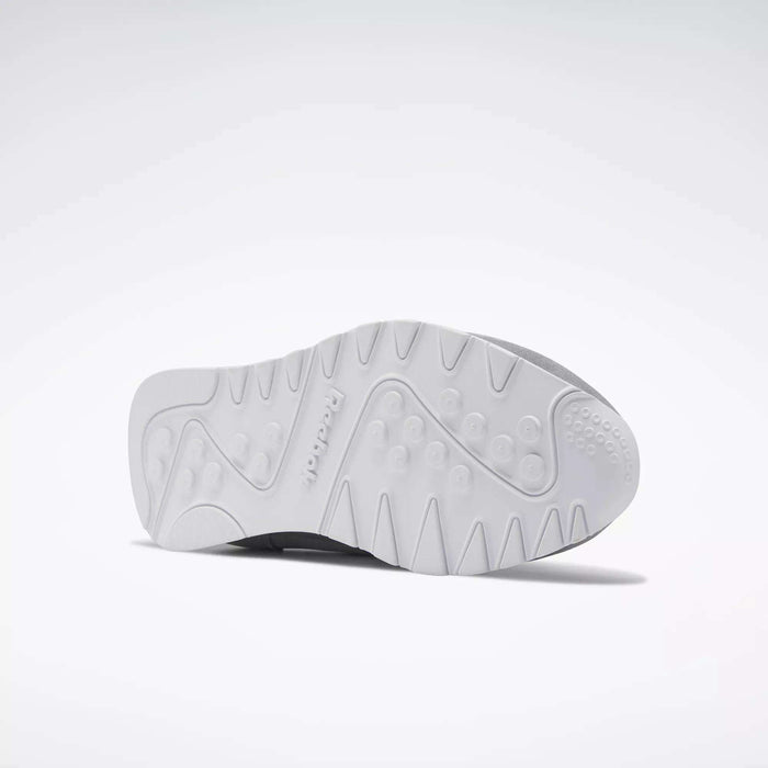 The image shows the sole of Reebok Men's Classic Nylon Shoes with a white rubber outsole featuring raised circular grips, textured patterns for traction, and an embossed Reebok logo in the center. The background is plain white.