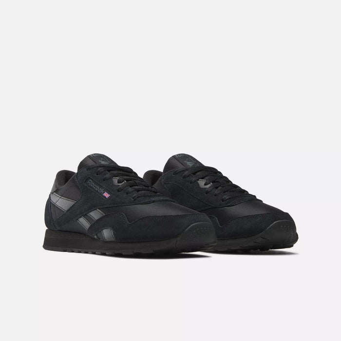 Men's Classic Nylon Shoes by Reebok feature a black nylon upper, black laces and soles, and a small British flag logo on the side. These classic everyday sneakers are shown against a plain white background.