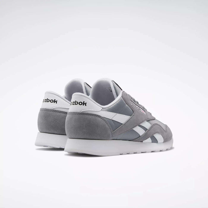 A pair of Reebok Men's Classic Nylon Shoes in gray and white are displayed on a white background, angled to highlight the iconic Reebok branding on the heel.