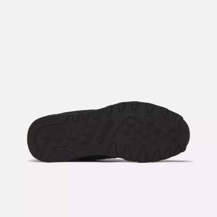 The image shows the black rubber outsole of Reebok Men's Classic Nylon Shoes, featuring a textured tread with circular and linear grooves for grip. The Reebok logo is embossed in the center of the sole.