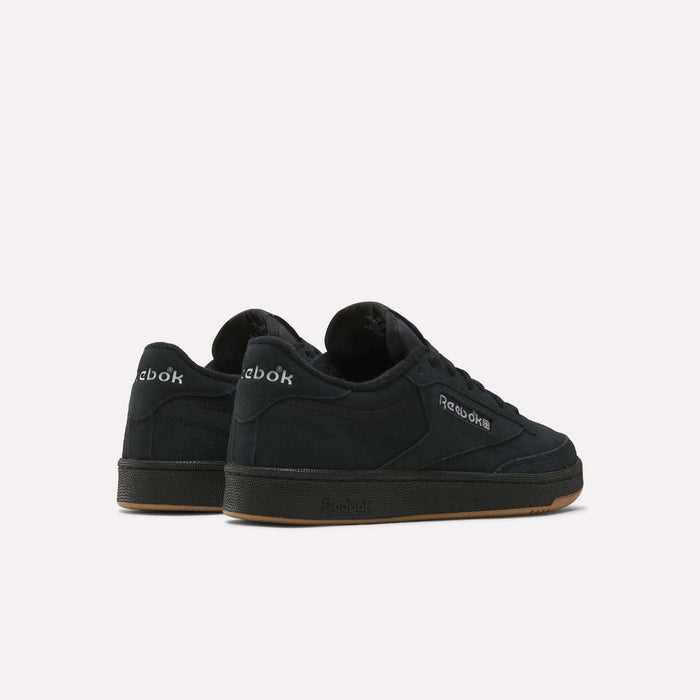 A pair of black Reebok Club C 85 Shoes with suede uppers and gum soles is displayed on a white background, one shoe facing forward and the other angled back, showcasing the court-inspired Reebok logos on the sides and heel.