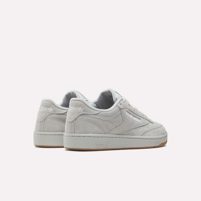 The Reebok Club C 85 Shoes feature a light gray suede upper, white laces, and beige rubber soles, displayed from an angled back and side view against a plain white background.