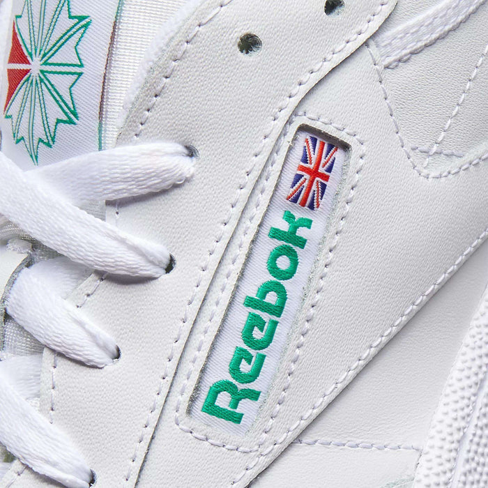 Close-up of Reebok Club C 85 Shoes in white leather, highlighting the green Reebok logo, small Union Jack flag on the side, white laces, and stitched details—classic tennis-inspired style.