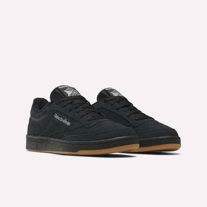 The Reebok Club C 85 Shoes in black feature a suede upper, gum rubber soles, and Reebok logos on the side and tongue, shown against a plain white background.