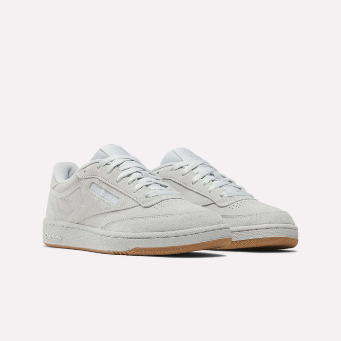 The Reebok Club C 85 Shoes feature a light gray suede upper, white laces, and gum rubber outsoles for a classic court look, highlighted against a plain white background.
