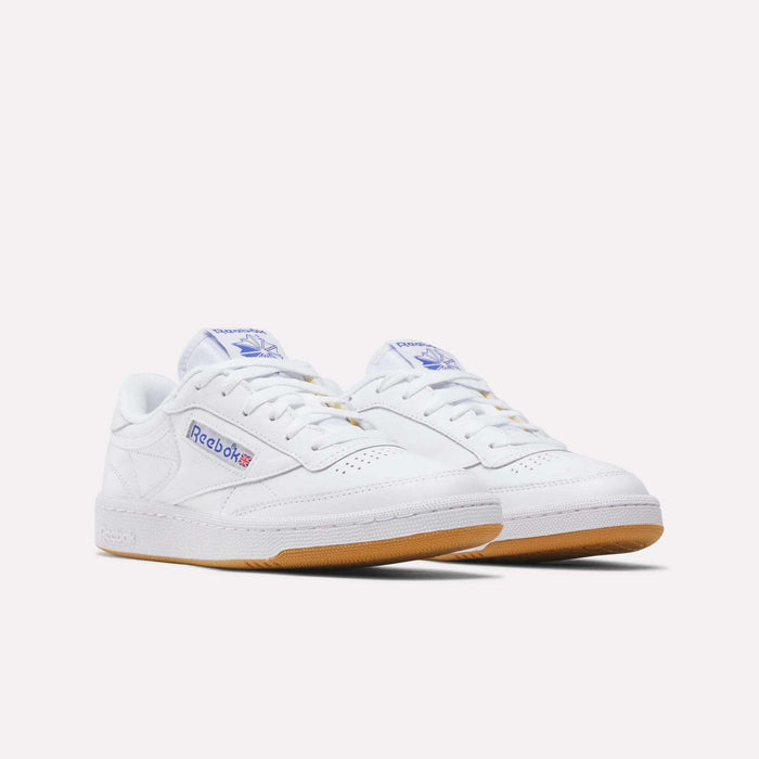 A pair of Reebok Club C 85 Shoes in white leather with gum soles, featuring blue Reebok branding on the side and tongue, and white laces. Displayed against a plain white background, these tennis-inspired sneakers offer classic style and comfort.