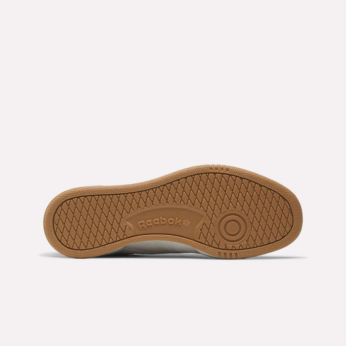The image shows the sole of a Reebok Club C 85 shoe, featuring a brown rubber outsole with a herringbone tread pattern and the Reebok logo embossed in the center.