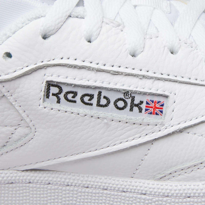 Close-up of Reebok Men's Club C 85 Shoes, featuring the stitched logo and Union Jack flag on the side, with visible leather texture and white laces.