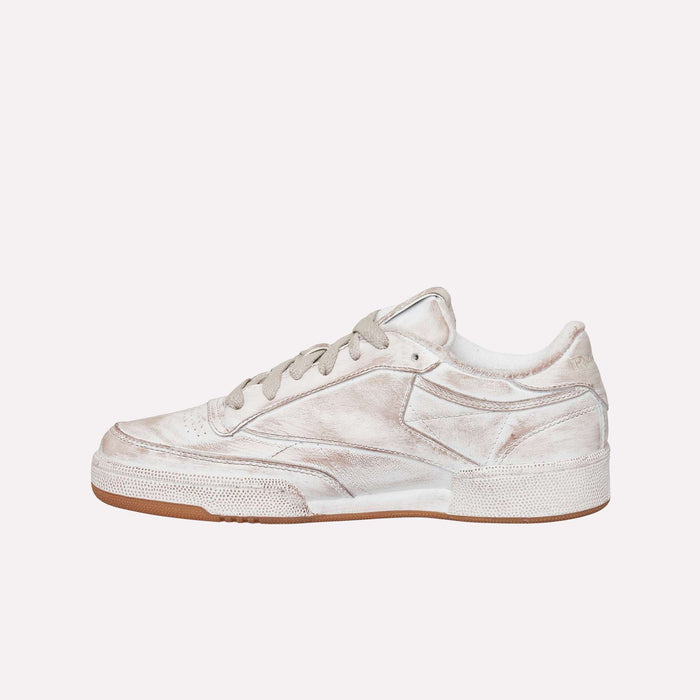 A worn, off-white Reebok Club C 85 Vintage LTD Shoe with a low-top silhouette, textured sole, and light brown outsole. The sneaker displays visible creases and scuffs, showcasing a minimalist design against a plain light background—capturing the essence of this iconic lifestyle tennis classic.