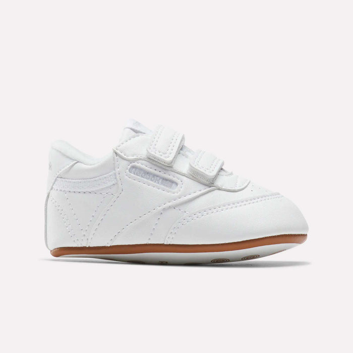 Reebok Kids' Club C Crib Shoes for toddlers feature a soft white leather upper, dual hook-and-loop closures, subtle stitching, and a light brown rubber sole, displayed against a plain white background.