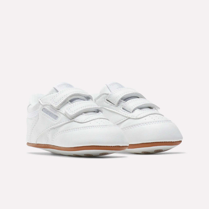 Reebok Kids' Club C Crib Shoes for babies and toddlers feature a soft white leather upper, hook-and-loop closures, and light brown rubber soles, displayed on a plain white background.