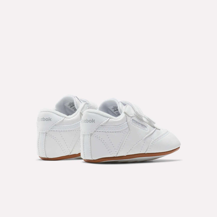 The Reebok Kids' Club C Crib Shoes for babies and toddlers feature a soft leather upper, white color, hook-and-loop closure, and brown rubber soles, shown on a plain white background.