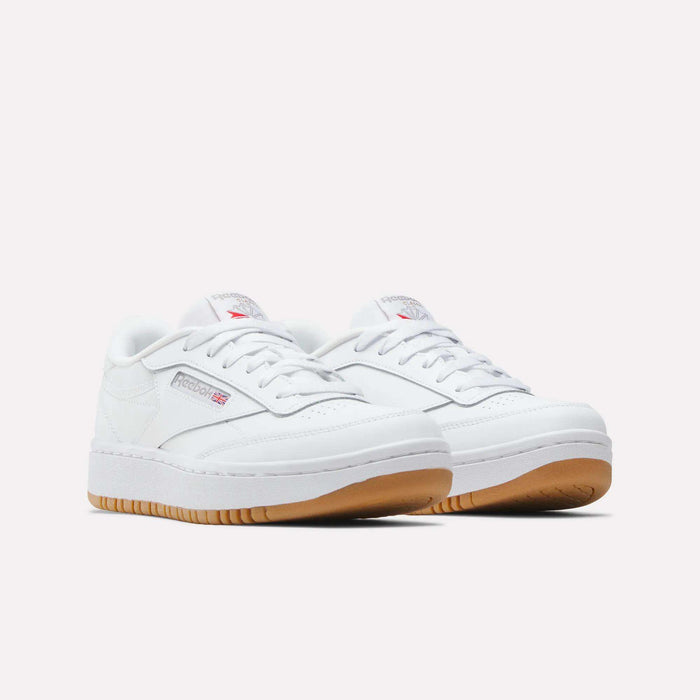 The Reebok Club C Double Shoes for Big Kids feature a white leather upper, low-top design, white laces, and gum rubber soles. Both the side and tongue display the Reebok logo, set against a plain light background.