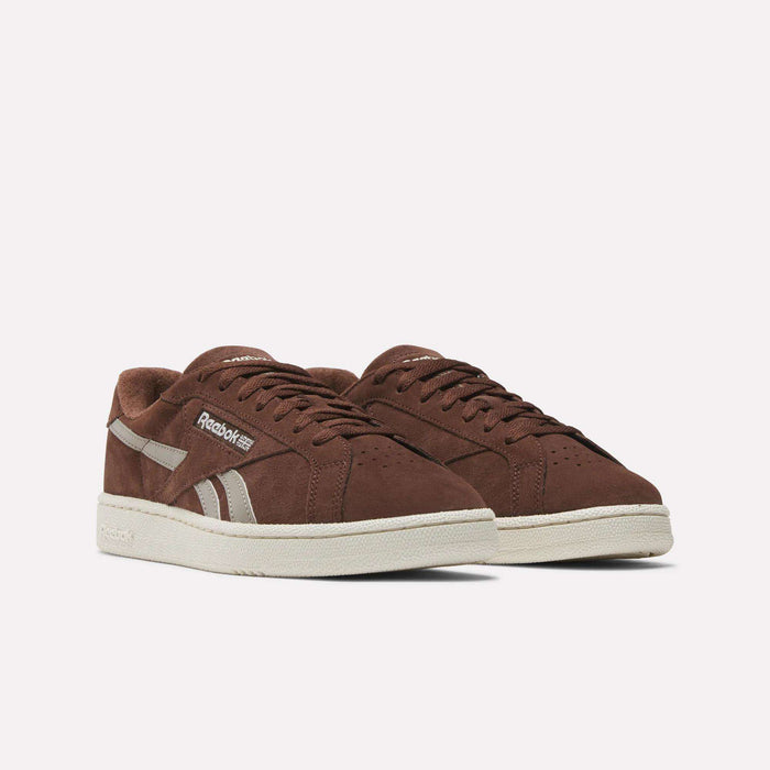 The Reebok Club C Grounds UK Shoes feature brown suede uppers, white accents, and off-white rubber soles, capturing the vintage charm of classic tennis sneakers. They are shown side by side against a plain white background.