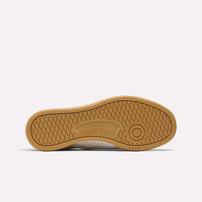 Bottom view of the Reebok Club C Grounds UK Shoes shows a tan rubber sole with a textured herringbone pattern and the Reebok logo embossed near the center, emphasizing its classic style.