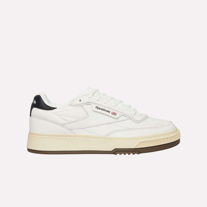 A white Reebok sneaker with a beige sole, black heel detail, and Reebok logo on the side, shown in a side profile on a plain white background.