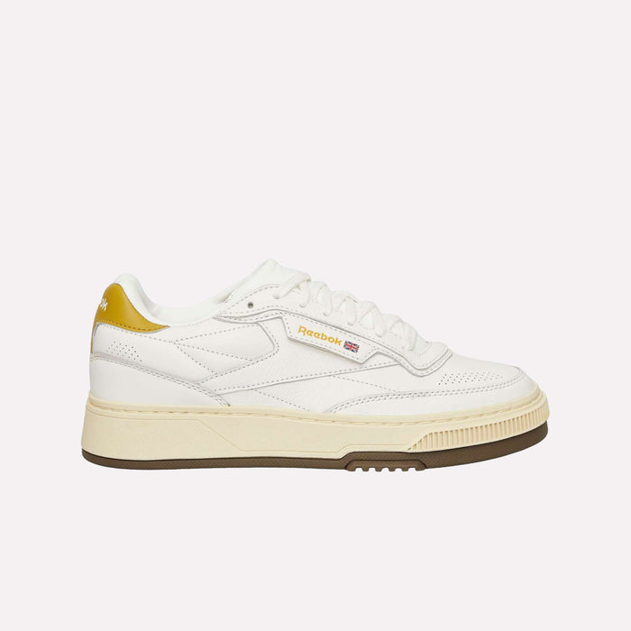 The Reebok Club C LTD Shoes, shown in profile on a plain white background, feature a clean white upper with a beige sole, yellow heel accent, and gold Reebok branding on the side—a lifestyle classic inspired by heritage tennis shoe design.