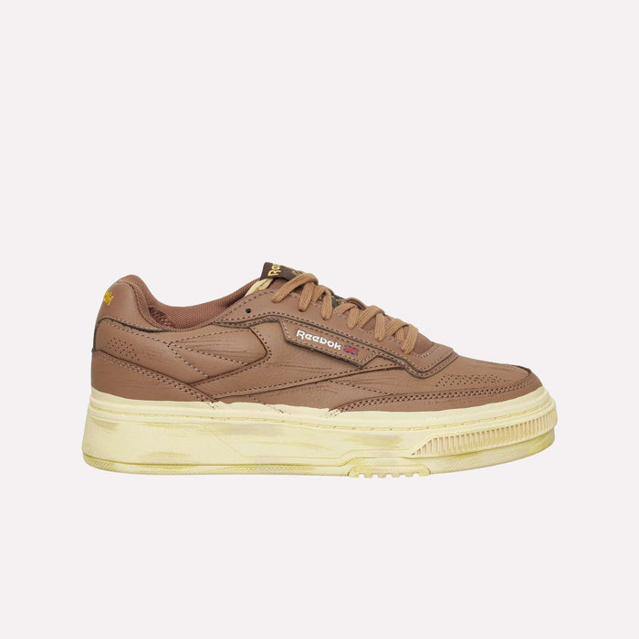 A side view of the Reebok Club C LTD Shoes in brown with a beige sole, set against a plain light background. This lifestyle classic showcases visible stitching and the Reebok logo on the side in yellow and red.