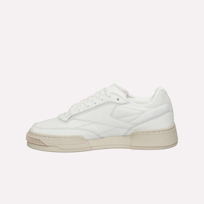 A white low-top tennis shoe with a beige sole, minimal stitching, and a clean design, the Reebok Club C LTD Shoes—echoing the timeless style of the classic Club C—are displayed on a plain white background.