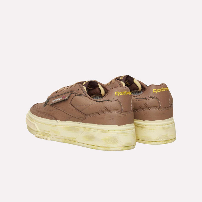 Brown Reebok Club C LTD Shoes with yellowed, worn-effect soles and yellow Reebok branding on the heel, displayed from a rear angle against a white background—a lifestyle classic that blends timeless tennis shoe style with everyday comfort.