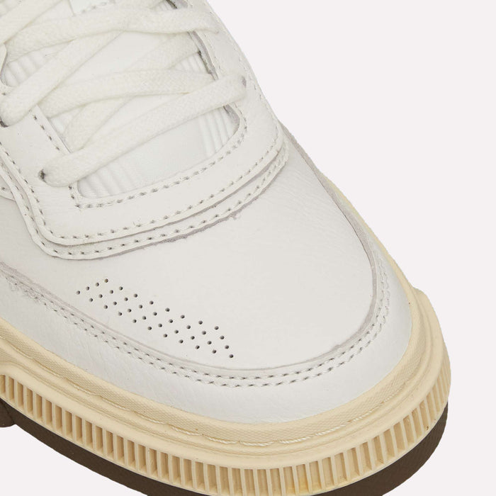 Close-up of the front and side of the Reebok Club C LTD Shoes, a white lifestyle classic sneaker featuring a cream-colored outsole, white laces, textured leather upper, and small perforations near the toe—showcasing the iconic Club C tennis shoe design.