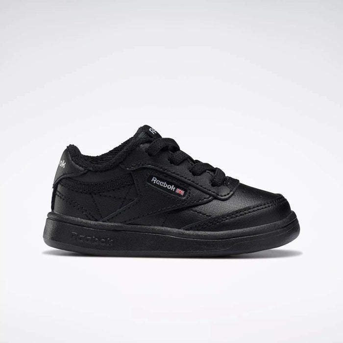 A side profile of the Reebok Kids' Club C Shoes for babies and toddlers is shown against a white background, featuring black soft leather, black laces, detailed stitching, and a small Reebok logo with British flag on the side.