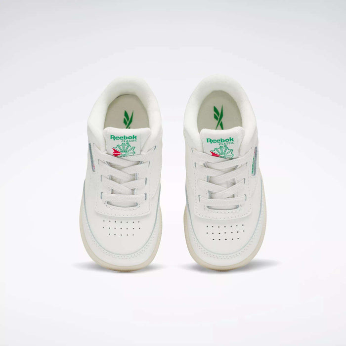 A pair of Reebok Kids' Club C Shoes for toddlers in white with green and pink accents, inspired by '80s style, shown from above on a plain background. Both shoes feature the Reebok logo and a leaf graphic on the tongue.