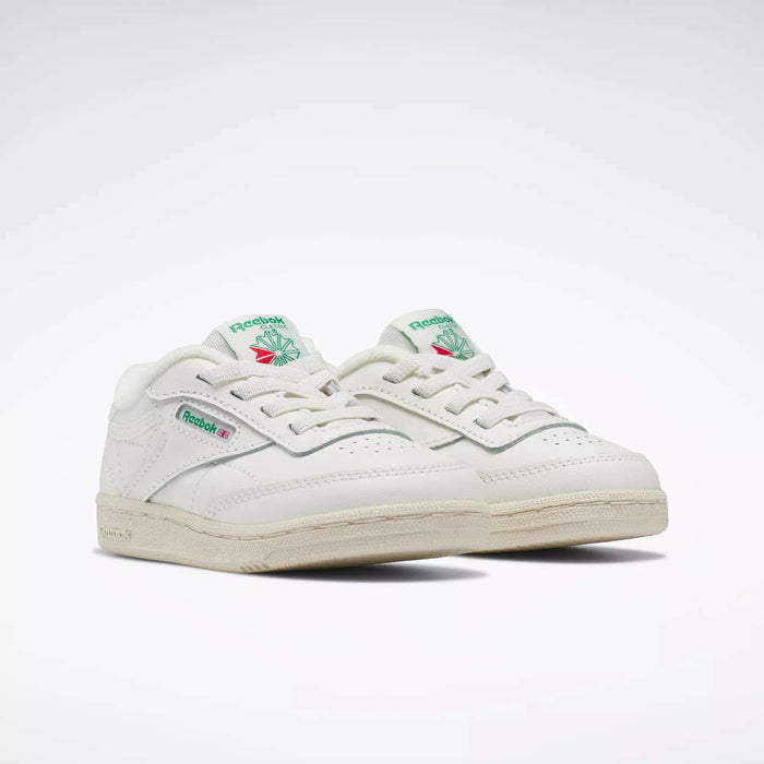 A pair of Reebok Kids' Club C Shoes for baby and toddler, white with green and pink logo accents, off-white soles, and a classic low-top ‘80s design, displayed side by side on a plain white background.