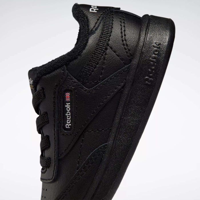 A close-up of Reebok Kids' Club C Shoes for babies and toddlers in black leather, showing the side profile with visible stitching, laces, the Reebok logo, and Union Jack tag. The shoe is angled upward on a plain white background.