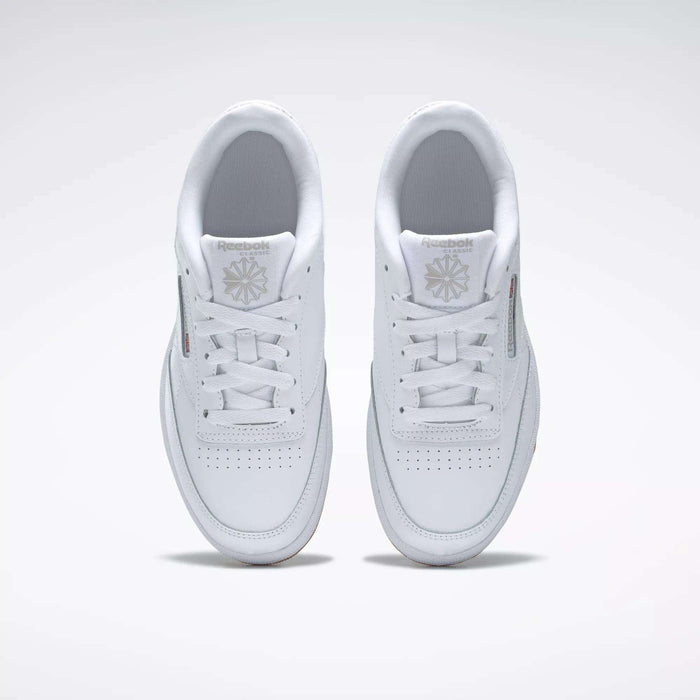 A pair of Kids' Club C Shoes - Grade School by Reebok, seen from above, with clean white leather uppers, laces, perforated toes, and Reebok logos on the tongues. The classic court style is displayed side by side on a light background.