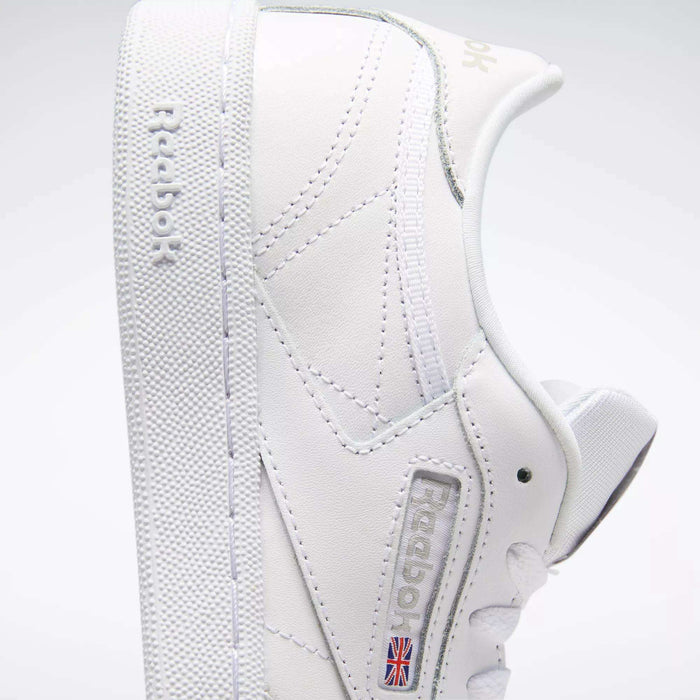 A close-up side view of the Reebok Kids' Club C Shoes - Grade School displays soft white leather uppers, clean minimal stitching, a textured sole, "Reebok" embossed on the side, and the Union Jack flag near the sole.