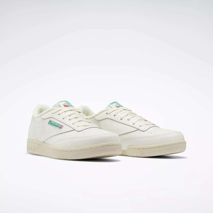 The Reebok Club C Shoes for big kids feature an off-white design with green and red logo details on the side and tongue, inspired by classic '80s style, set against a plain white background.