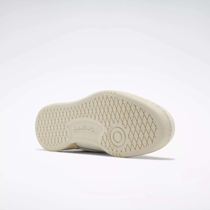 A beige Reebok Club C Shoe for big kids lies on its side, highlighting the diamond-patterned textured rubber outsole and embossed Reebok logo—an iconic ’80s-inspired design.