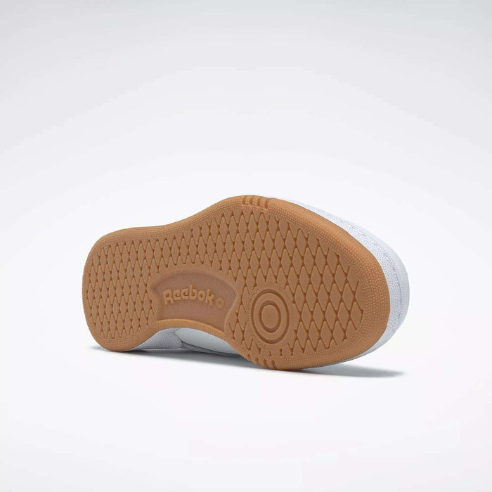 The image shows the underside of a white Reebok Kids' Club C Shoe - Grade School, featuring a high-abrasion rubber outsole with the Reebok logo and a circular pattern near the ball of the foot, classic to court shoes.