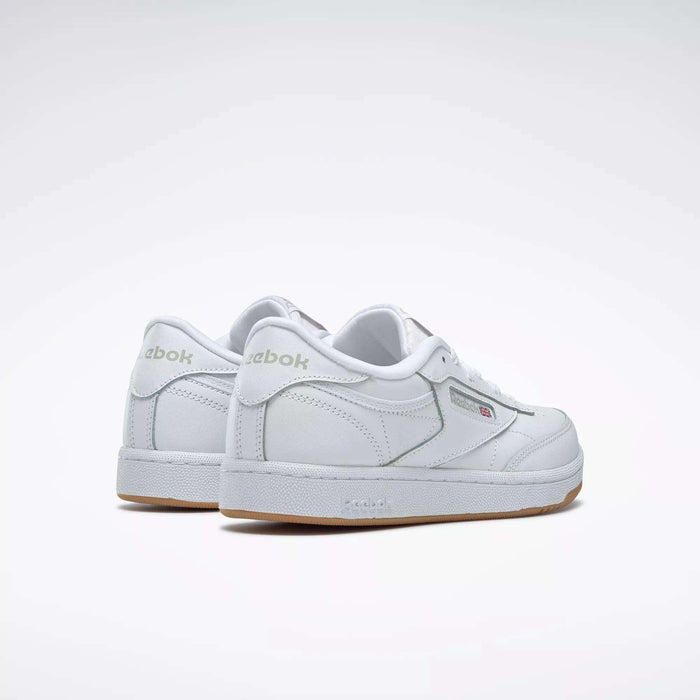 The Reebok Kids' Club C Shoes – Grade School feature soft white leather uppers, subtle grey branding, and a gum sole. Shown on a light background, the sneakers are angled to highlight the back and side views.