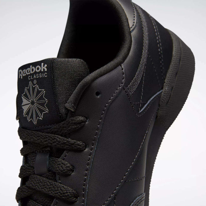 Close-up of black Reebok Kids' Club C Shoes (Grade School), featuring smooth leather uppers, the tongue with Reebok logo and starburst design, black laces, and detailed stitching.